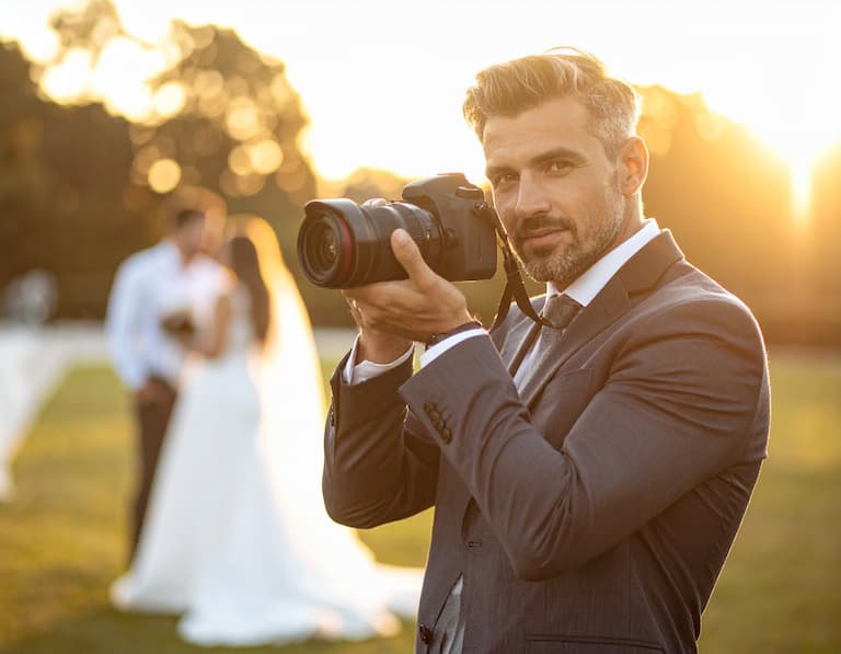Un photographe professionnel avec son équipement, capturant une séance de couple lors d'un mariage en extérieur au coucher du soleil